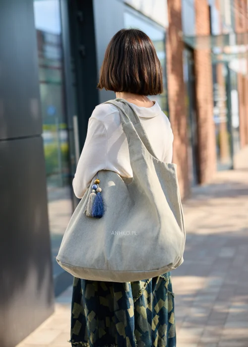 Duża beżowa torba typu shopper z miękkiej tkaniny z ozdobnym chwostem i drewnianymi koralikami.