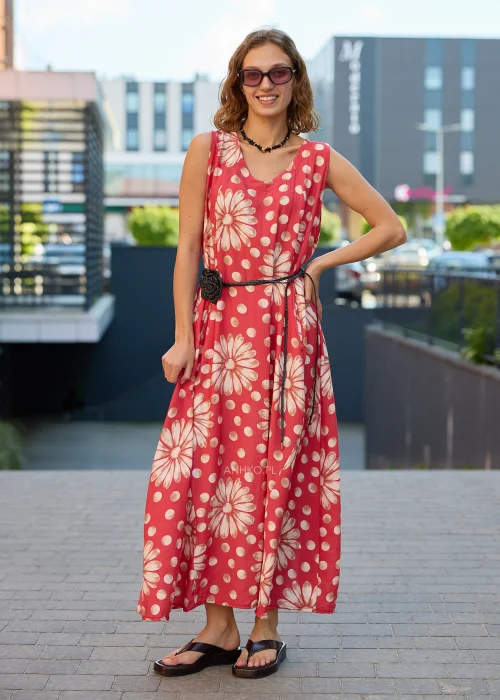 Sukienka maxi Plus Size w koralowym kolorze z dużym kwiatowym wzorem i białymi groszkami, z okrągłym dekoltem, kieszeniami i ozdobnym paskiem w talii, prezentowana w miejskiej stylizacji.