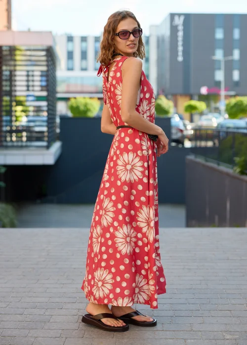 Sukienka maxi Plus Size w koralowym kolorze z dużym kwiatowym wzorem i białymi groszkami, z okrągłym dekoltem, kieszeniami i ozdobnym paskiem w talii, prezentowana w miejskiej stylizacji.