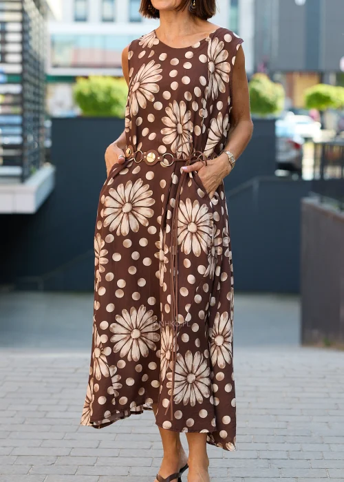 Sukienka maxi Plus Size w brązowym kolorze z dużym kwiatowym wzorem i białymi groszkami, z okrągłym dekoltem, kieszeniami i ozdobnym paskiem w talii, prezentowana w miejskiej stylizacji.