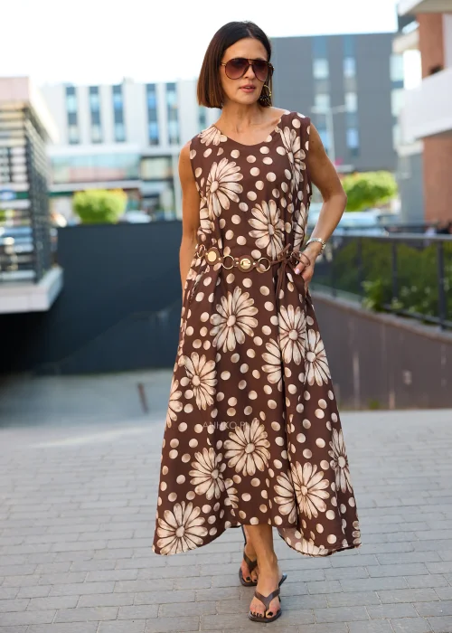 Sukienka maxi Plus Size w brązowym kolorze z dużym kwiatowym wzorem i białymi groszkami, z okrągłym dekoltem, kieszeniami i ozdobnym paskiem w talii, prezentowana w miejskiej stylizacji.