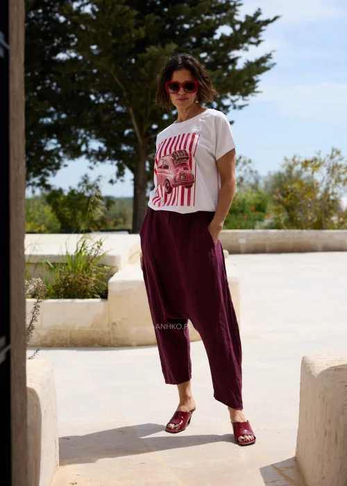 Biały damski T-shirt z czerwonym nadrukiem retro samochodu i pionowymi pasami, w zestawieniu z bordowymi spodniami o luźnym fasonie.