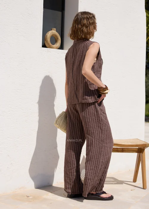 Brązowa lniana kamizelka damska w białe paski z klapami i guzikami, zestawiona z pasującymi spodniami, tworzy elegancki komplet w stylu casual.