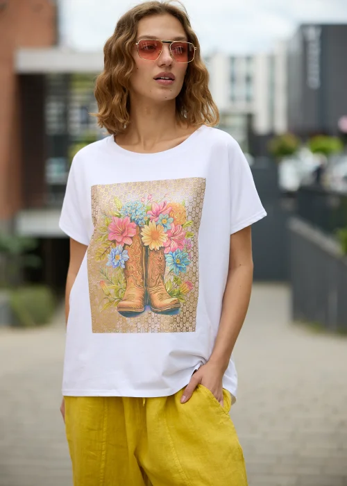 Biały t-shirt damski z efektownym nadrukiem kowbojskich botków wypełnionych kolorowymi kwiatami na beżowym tle.
