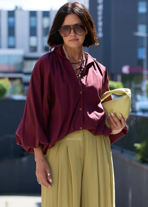 Bordowa koszula oversize z bufiastymi rękawami, zestawiona z oliwkowymi szerokimi spodniami i jasną kopertówką w eleganckiej stylizacji