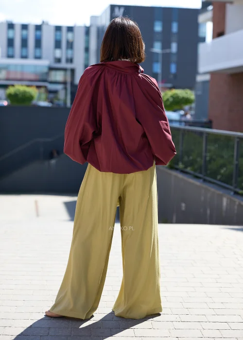 Bordowa koszula oversize z bufiastymi rękawami, zestawiona z oliwkowymi szerokimi spodniami i jasną kopertówką w eleganckiej stylizacji