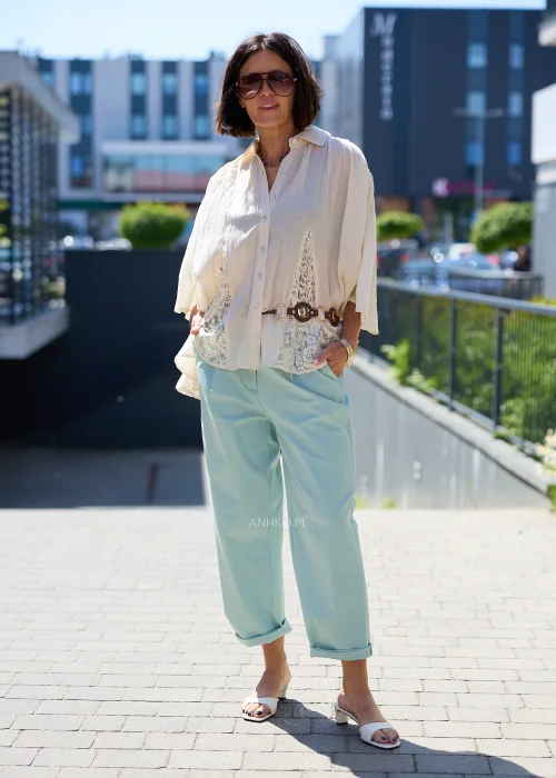 Biała oversize bluzka z koronkowym dołem i szerokimi rękawami, zapinana na guziki, zestawiona z miętowymi spodniami w lekkiej eleganckiej stylizacji