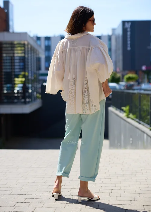 Biała oversize bluzka z koronkowym dołem i szerokimi rękawami, zapinana na guziki, zestawiona z miętowymi spodniami w lekkiej eleganckiej stylizacji