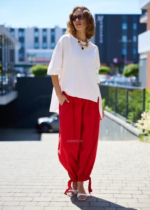 Biała bluzka oversize damska z asymetrycznym dołem i rękawem 3/4 w eleganckiej stylizacji z czerwonymi spodniami