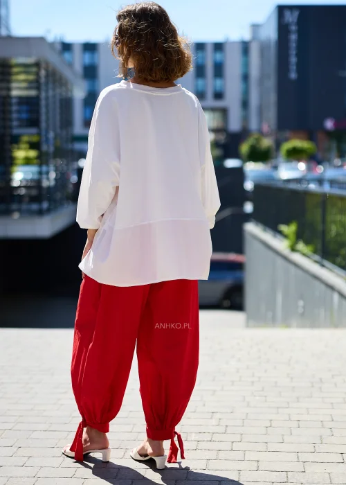 Biała bluzka oversize damska z asymetrycznym dołem i rękawem 3/4 w eleganckiej stylizacji z czerwonymi spodniami