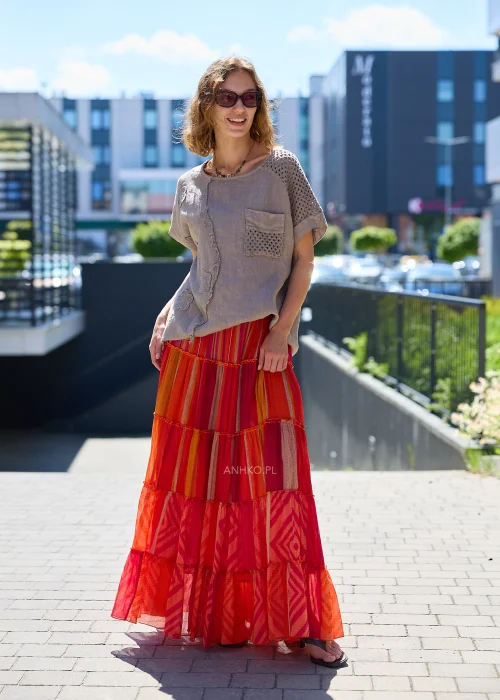 Spódnica maxi z falbanami w odcieniach czerwieni, różu i pomarańczu z patchworkowym wzorem, zestawiona z plecioną torebką w stylu boho.