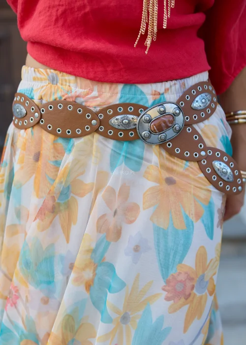 Brązowy szeroki pasek damski z dużą ozdobną klamrą z imitacją kamienia, metalowymi aplikacjami i dekoracyjnymi oczkami. Styl western i boho doskonale uzupełnia sukienki, tuniki oraz jeansowe stylizacje.