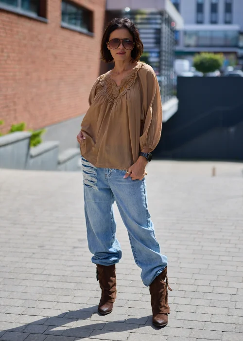 Camelowa bluzka damska z haftem przy dekolcie V i luźnym krojem, zestawiona z jasnymi jeansami w stylizacji casual.