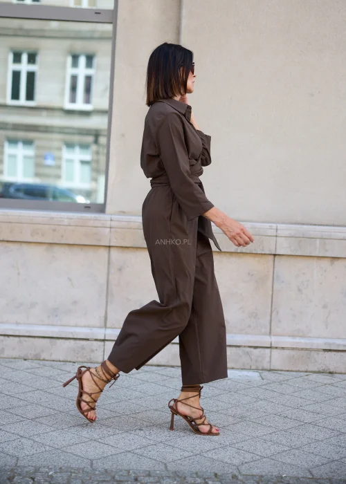 Damski kombinezon kopertowy w kolorze czekoladowego brązu z kołnierzykiem, wiązaniem w talii i szerokimi nogawkami, elegancki fason na obcasach.