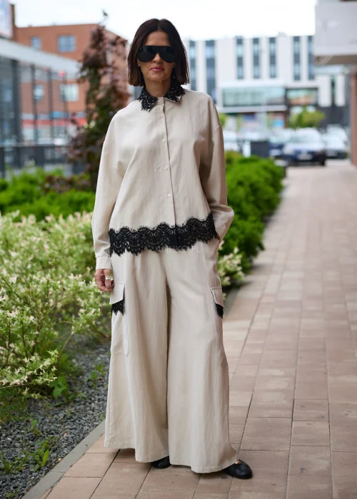 Koszula oversize w kolorze beżowym z czarną koronką przy kołnierzu i dole, o luźnym kroju z długim rękawem, stylizowana w elegancko-nowoczesnym zestawie.