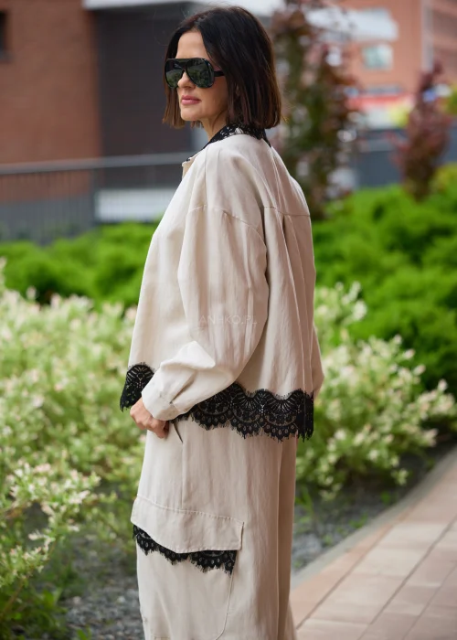 Koszula oversize w kolorze beżowym z czarną koronką przy kołnierzu i dole, o luźnym kroju z długim rękawem, stylizowana w elegancko-nowoczesnym zestawie.
