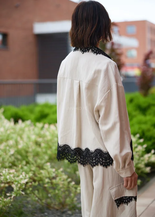 Koszula oversize w kolorze beżowym z czarną koronką przy kołnierzu i dole, o luźnym kroju z długim rękawem, stylizowana w elegancko-nowoczesnym zestawie.