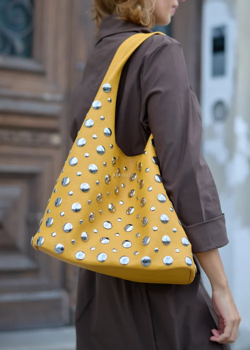Musztardowa torebka damska typu shopper o ziarnistej powierzchni, z szerokim uchwytem i licznymi srebrnymi ćwiekami w różnych rozmiarach.
