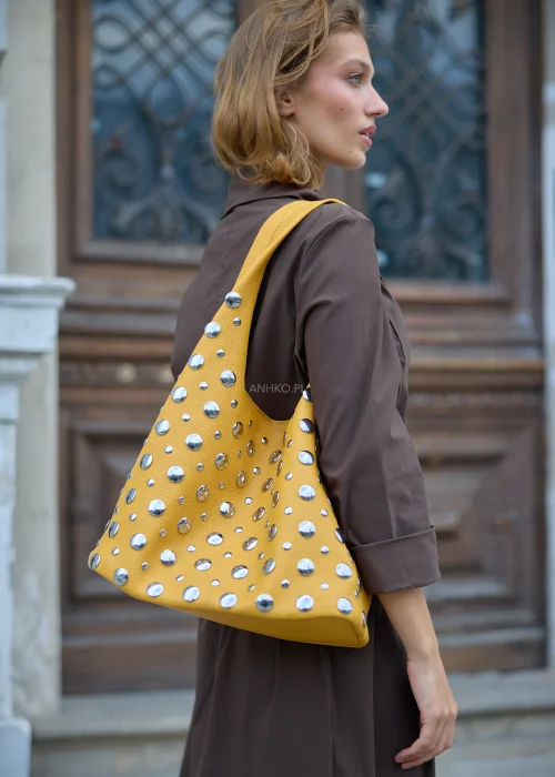 Musztardowa torebka damska typu shopper o ziarnistej powierzchni, z szerokim uchwytem i licznymi srebrnymi ćwiekami w różnych rozmiarach.