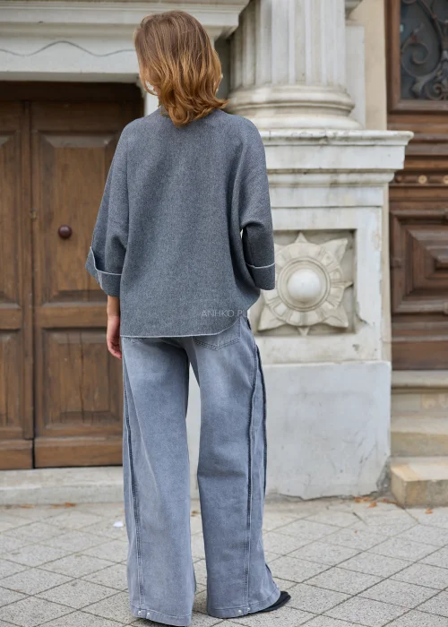 Szary sweter damski oversize z półgolfem, rękawami 3/4 i kontrastowymi czarno-białymi paskami, zestawiony z szarymi jeansami.