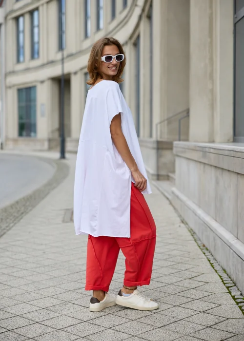 Bluzka damska w białym kolorze, o mocno oversize’owym fasonie z krótkimi rękawami, wydłużonymi bokami i asymetrycznym dołem.