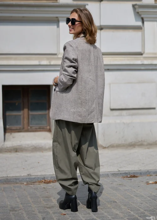 Khaki spodnie damskie o luźnym fasonie z szerokimi nogawkami, elastyczną talią i długim troczkiem, stylizowane z beżową bluzką i czarnymi botkami.