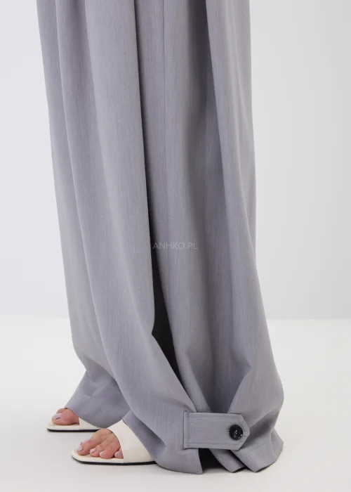Szare spodnie damskie wide leg z szerokimi nogawkami i ozdobnymi patkami z guzikami przy dole nogawek.