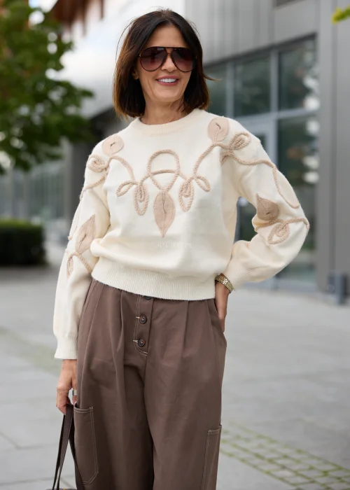 Sweter damski w kolorze ecru, z okrągłym dekoltem, długimi rękawami i beżową aplikacją roślinną 3D.
