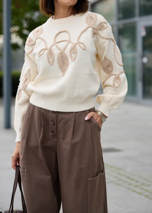 Sweter damski w kolorze ecru, z okrągłym dekoltem, długimi rękawami i beżową aplikacją roślinną 3D.
