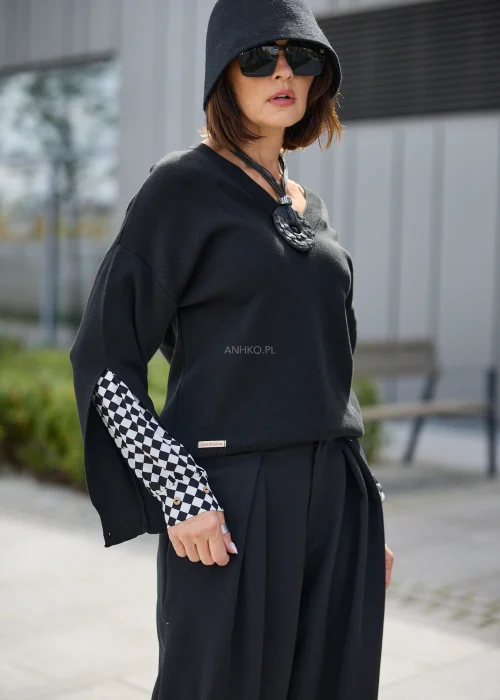 Sweter damski oversize w czarnym kolorze, z dekoltem V i rozcięciami na rękawach odsłaniającymi czarno-białą kratę.