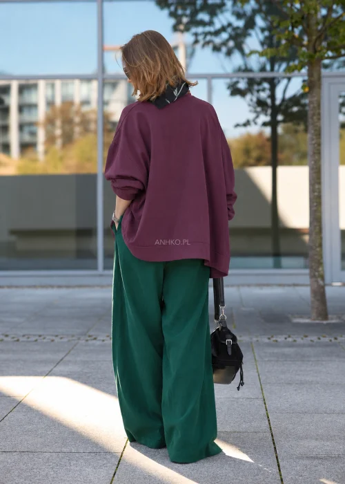 Bluzka damska oversize w kolorze śliwkowego fioletu, z luźnym, szerokim fasonem, obniżoną linią ramion, długimi rękawami, asymetrycznym warstwowym dołem oraz dekoracyjnymi wiązaniami po bokach.