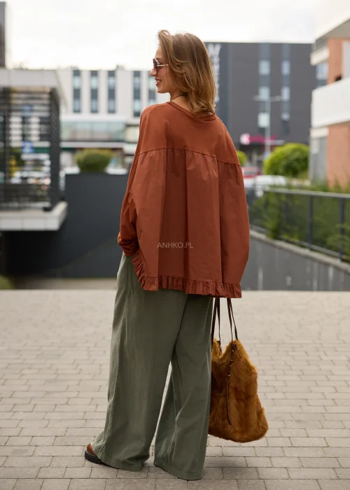 Bluzka damska oversize w kolorze rdzawobrązowym, o bardzo luźnym fasonie, z okrągłym dekoltem, mocno obniżoną linią ramion, długimi szerokimi rękawami oraz asymetrycznym, wydłużonym tyłem wykończonym marszczoną falbaną.