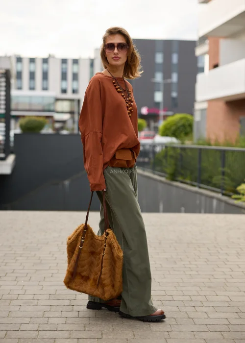 Bluzka damska oversize w kolorze rdzawobrązowym, o bardzo luźnym fasonie, z okrągłym dekoltem, mocno obniżoną linią ramion, długimi szerokimi rękawami oraz asymetrycznym, wydłużonym tyłem wykończonym marszczoną falbaną.