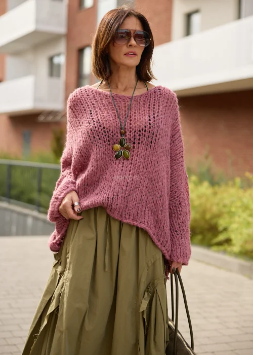 Sweter damski oversize w pudrowym różu, o ażurowym splocie, szerokich rękawach i luźnym, asymetrycznym fasonie.