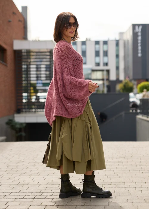Sweter damski oversize w pudrowym różu, o ażurowym splocie, szerokich rękawach i luźnym, asymetrycznym fasonie.