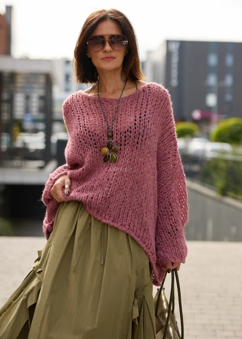 Sweter damski oversize w pudrowym różu, o ażurowym splocie, szerokich rękawach i luźnym, asymetrycznym fasonie.