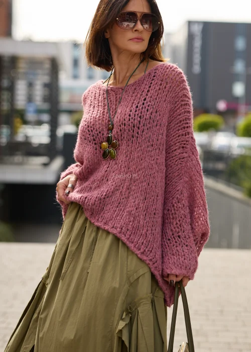 Sweter damski oversize w pudrowym różu, o ażurowym splocie, szerokich rękawach i luźnym, asymetrycznym fasonie.