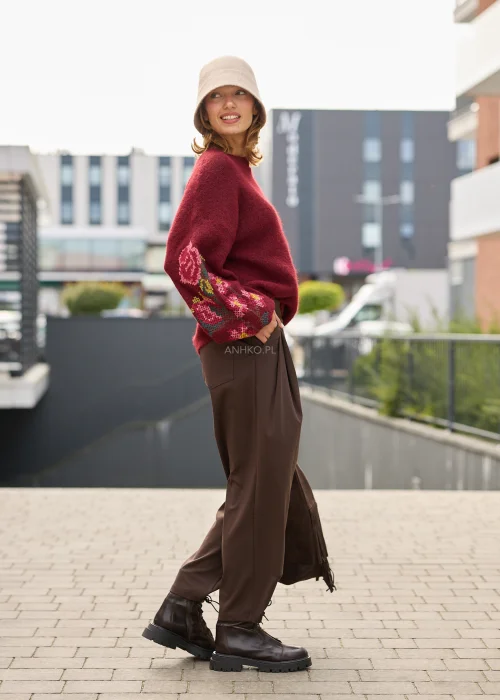 Sweter damski oversize w bordowym kolorze, z szerokimi rękawami ozdobionymi kolorowym haftem w kwiatowe motywy.