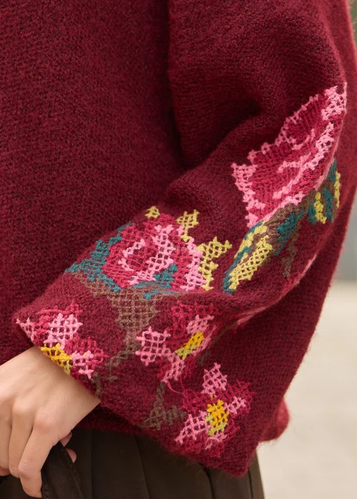 Sweter damski oversize w bordowym kolorze, z szerokimi rękawami ozdobionymi kolorowym haftem w kwiatowe motywy.