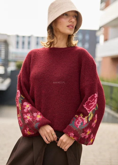 Sweter damski oversize w bordowym kolorze, z szerokimi rękawami ozdobionymi kolorowym haftem w kwiatowe motywy.
