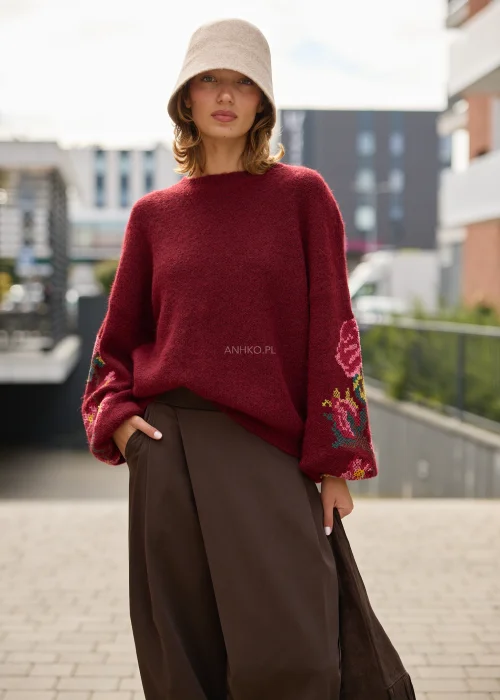 Sweter damski oversize w bordowym kolorze, z szerokimi rękawami ozdobionymi kolorowym haftem w kwiatowe motywy.
