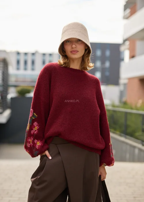 Sweter damski oversize w bordowym kolorze, z szerokimi rękawami ozdobionymi kolorowym haftem w kwiatowe motywy.