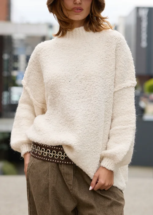 Dzianinowy sweter damski oversize w kremowym kolorze, o miękkiej, wyraźnie teksturowanej strukturze, z obniżoną linią ramion, długimi rękawami i prostym dekoltem pod szyję.