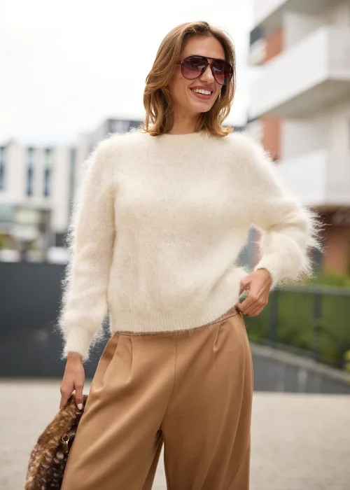 Puszysty sweter damski w kremowym kolorze, o luźnym fasonie, z okrągłym dekoltem, długimi rękawami i miękką, włochatą fakturą dzianiny.