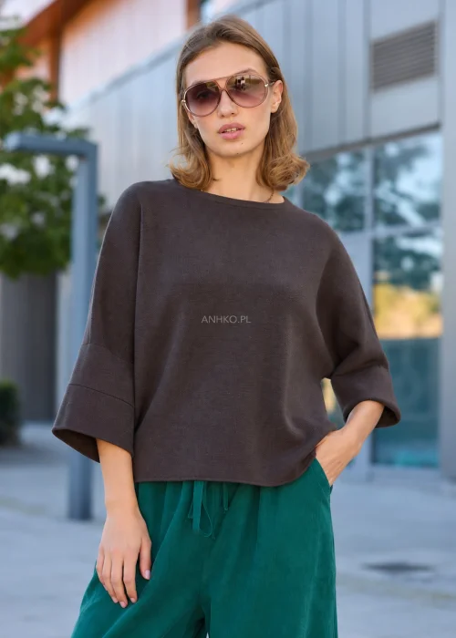Dzianinowy sweter damski oversize w ciemnobrązowym kolorze, z szerokim fasonem, obniżoną linią ramion i luźnymi rękawami o długości 3/4.