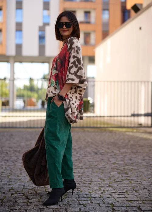 Sweter damski oversize typu ponczo z miękkiej, lekko puszystej dzianiny w kolorze beżowym, z wyrazistym nadrukiem dużych czerwonych kwiatów, zielonych liści oraz brązowych cętek w stylu panterki