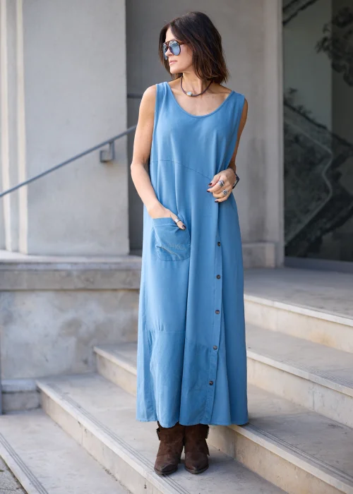 Sukienka damska maxi w kolorze przygaszonego błękitu, o mocno oversize’owym fasonie, z długimi rękawami, okrągłym dekoltem, asymetryczną warstwą materiału, pionowym rzędem guzików i dużą naszywaną kieszenią.
