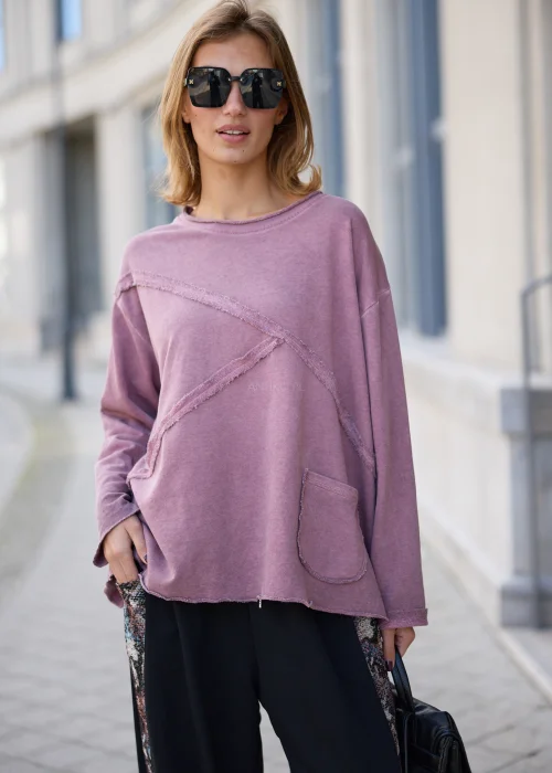Bluza damska oversize w odcieniu brudnego różu z efektem sprania, z okrągłym dekoltem, obniżoną linią ramion, długimi rękawami, asymetrycznymi przeszyciami o postrzępionych krawędziach oraz naszywaną kieszenią z przodu.