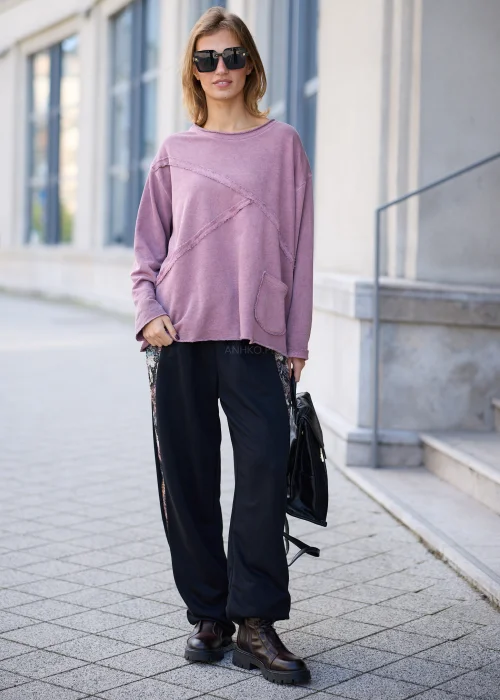 Bluza damska oversize w odcieniu brudnego różu z efektem sprania, z okrągłym dekoltem, obniżoną linią ramion, długimi rękawami, asymetrycznymi przeszyciami o postrzępionych krawędziach oraz naszywaną kieszenią z przodu.