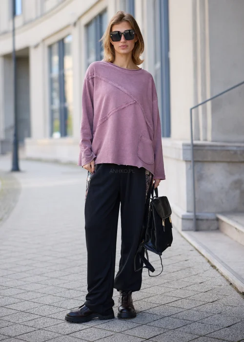 Bluza damska oversize w odcieniu brudnego różu z efektem sprania, z okrągłym dekoltem, obniżoną linią ramion, długimi rękawami, asymetrycznymi przeszyciami o postrzępionych krawędziach oraz naszywaną kieszenią z przodu.